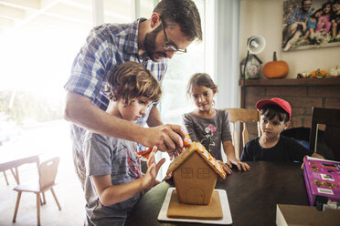 Familie dekoriert Lebkuchenhaus zu Hause - CAVF11058