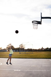 Girl throwing basketball to make a goal on court against sky - CAVF11074