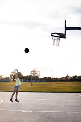 Mädchen wirft Basketball, um ein Tor auf dem Platz gegen den Himmel zu machen - CAVF11074