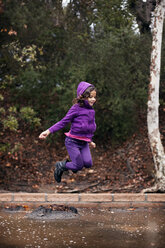 Happy girl jumping over puddle at field - CAVF11080