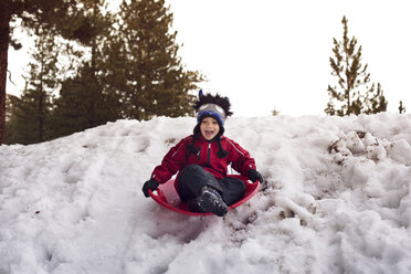 Boy screaming while tobogganing on sled at snowfield - CAVF11086