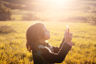 Side view of girl photographing through tablet computer while standing on grassy field - CAVF11092