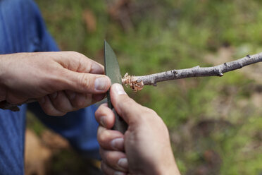 Ausgeschnittenes Bild eines Mannes, der im Wald einen Stock mit einem Messer schneidet - CAVF11113