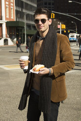 Porträt eines Mannes mit Kaffee und Hot Dog auf einer Straße in der Stadt - CAVF11164