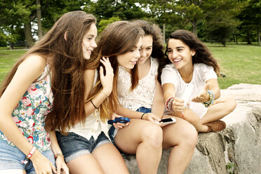 Teenage girl showing mobile phone to female friends while sitting at park - CAVF11190