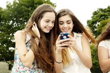 Female friends smiling while looking at mobile phone - CAVF11191