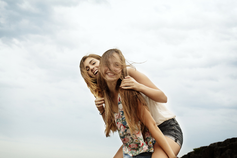 Teenager-Mädchen nimmt Freundin huckepack gegen den Himmel, lizenzfreies Stockfoto