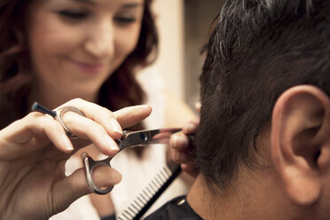 Nahaufnahme einer Friseurin, die einem männlichen Kunden im Salon die Haare schneidet - CAVF11234