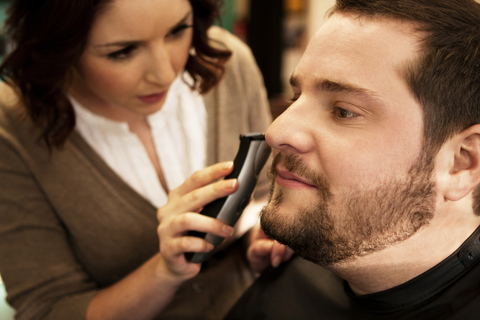 Nahaufnahme einer Friseurin, die den Bart eines männlichen Kunden im Salon stutzt, lizenzfreies Stockfoto