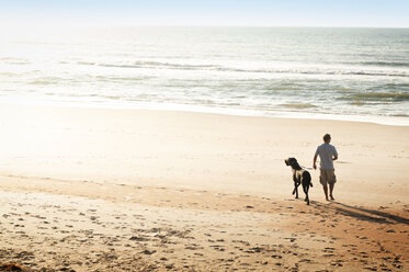 Rear view of man with dog walking at beach - CAVF11247