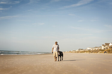 Man walking with dog on shore against sky - CAVF11251