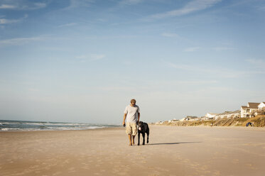 Mann spaziert mit Hund am Ufer gegen den Himmel - CAVF11251