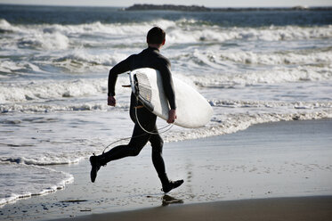 Rückansicht eines Surfers, der ein Surfbrett trägt, während er am Strand läuft - CAVF11269