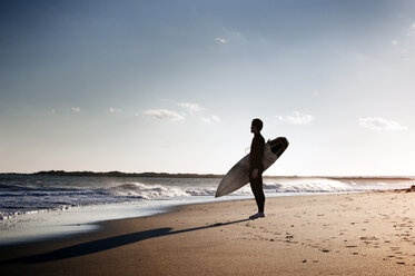 Seitenansicht eines Surfers, der ein Surfbrett trägt, während er am Ufer des Strandes steht - CAVF11275