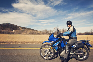 Porträt eines Motorradfahrers auf einem Motorrad sitzend vor bewölktem Himmel - CAVF11293