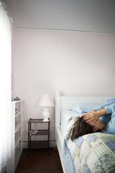 Frau, die ihr Gesicht mit den Händen bedeckt, während sie auf dem Bett liegt - CAVF11613
