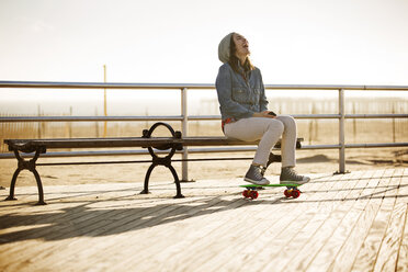 Woman laughing while sitting on bench at boardwalk - CAVF11629