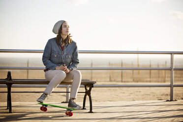 Woman listening music while sitting on bench at boardwalk - CAVF11630