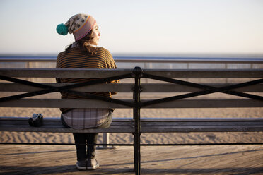 Rückansicht einer Frau, die auf einer Bank am Strand sitzt - CAVF11631