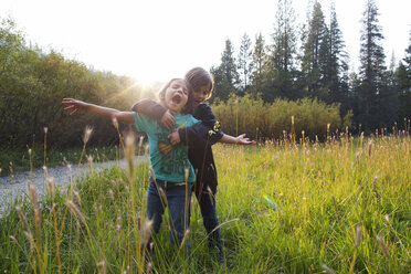 Girl embracing friend while standing on grass against sky - CAVF11656