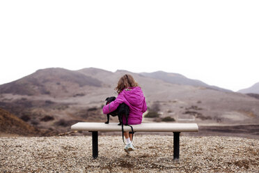 Rückansicht eines Mädchens, das auf einer Bank sitzend einen Hund hält, gegen einen klaren Himmel - CAVF11670