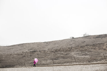 Fernblick auf ein Mädchen, das mit einem Regenschirm auf einem Feld gegen den klaren Himmel läuft - CAVF11687