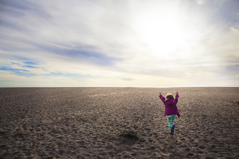 Rückansicht eines Mädchens, das auf Sand gegen einen bewölkten Himmel läuft, lizenzfreies Stockfoto