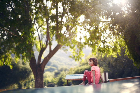 Mädchen sitzt auf Trampolin und schaut weg, lizenzfreies Stockfoto