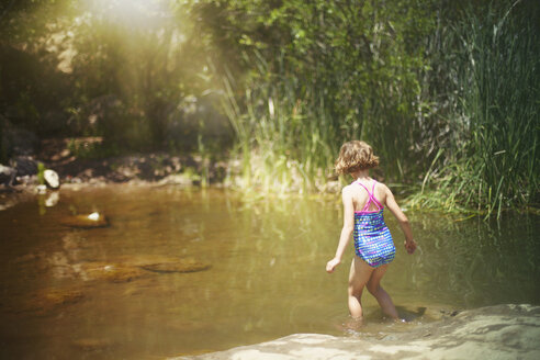 Rear view of girl walking in water at forest - CAVF11719