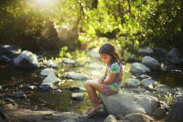 Nachdenkliches Mädchen, das auf einem Felsen am Fluss sitzt und nach unten schaut - CAVF11721