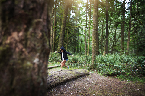 Verspieltes Mädchen läuft auf umgestürztem Baum im Wald, lizenzfreies Stockfoto