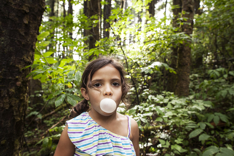 Porträt eines Mädchens, das im Wald Kaugummi bläst, lizenzfreies Stockfoto