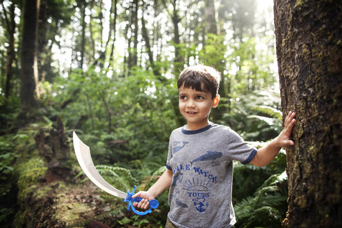 Boy holding toy sword while standing in forest - CAVF11762