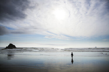 Boy walking on shore at beach against cloudy sky - CAVF11766
