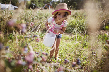 Portrait of girl watering plants in field - CAVF11771