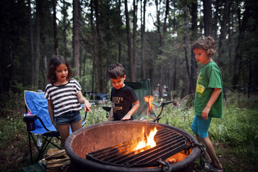 Children standing around fire pit in forest - CAVF11783