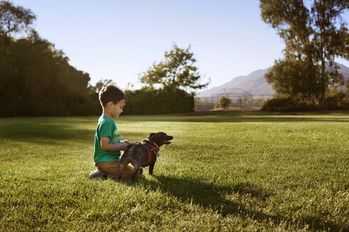 Junge mit Hund kniend auf einer Wiese im Park - CAVF11801