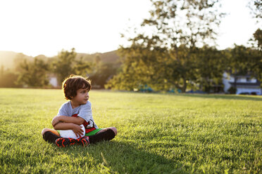 Boy sitting with soccer ball on grassy field at park - CAVF11812