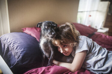 Girl embracing dog while lying on bed at home - CAVF11856