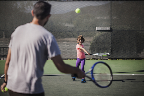 Vater und Tochter spielen Tennis auf dem Platz, lizenzfreies Stockfoto