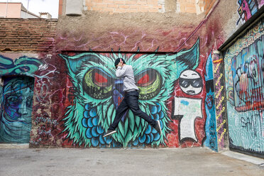 Young man with headphones jumping in the air in front of graffiti - AFVF00321