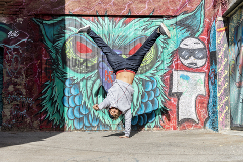 Junger Mann mit Kopfhörern macht Handstand vor einem Graffiti, lizenzfreies Stockfoto