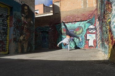 Young man doing handstand on one hand in front of graffiti - AFVF00324