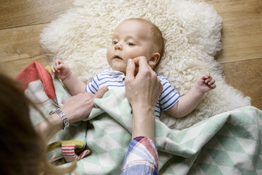Mother touching newborn baby's face, lying on lambskin - BMOF00040