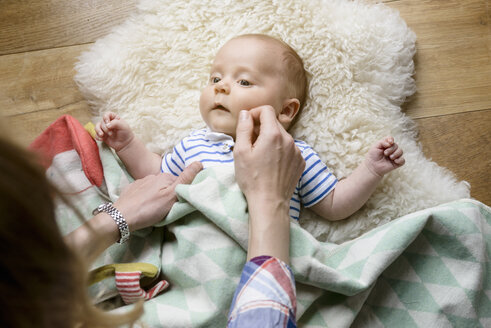 Mutter berührt das Gesicht ihres neugeborenen Babys, das auf einem Lammfell liegt - BMOF00040