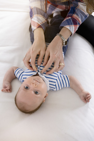 Mother dressing baby boy on couch stock photo