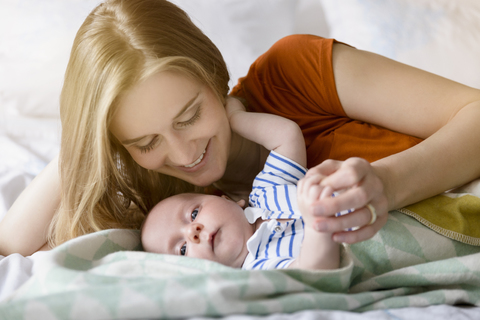 Smiling mother looking at her baby boy lying on bed stock photo