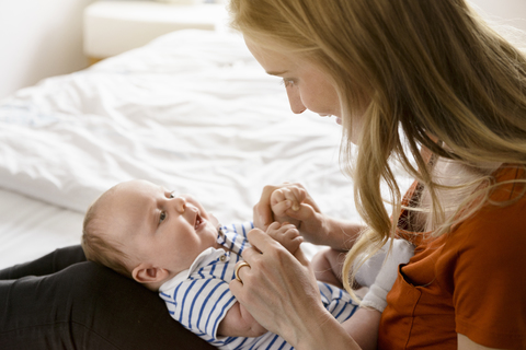 Smiling mother holding baby boy in lap on bed stock photo