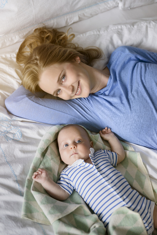 Portrait of smiling mother with her baby boy lying on bed stock photo