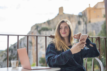 Spanien, Alquezar, Porträt einer entspannten jungen Frau mit Laptop und Mobiltelefon auf einer Terrasse sitzend - AFVF00337